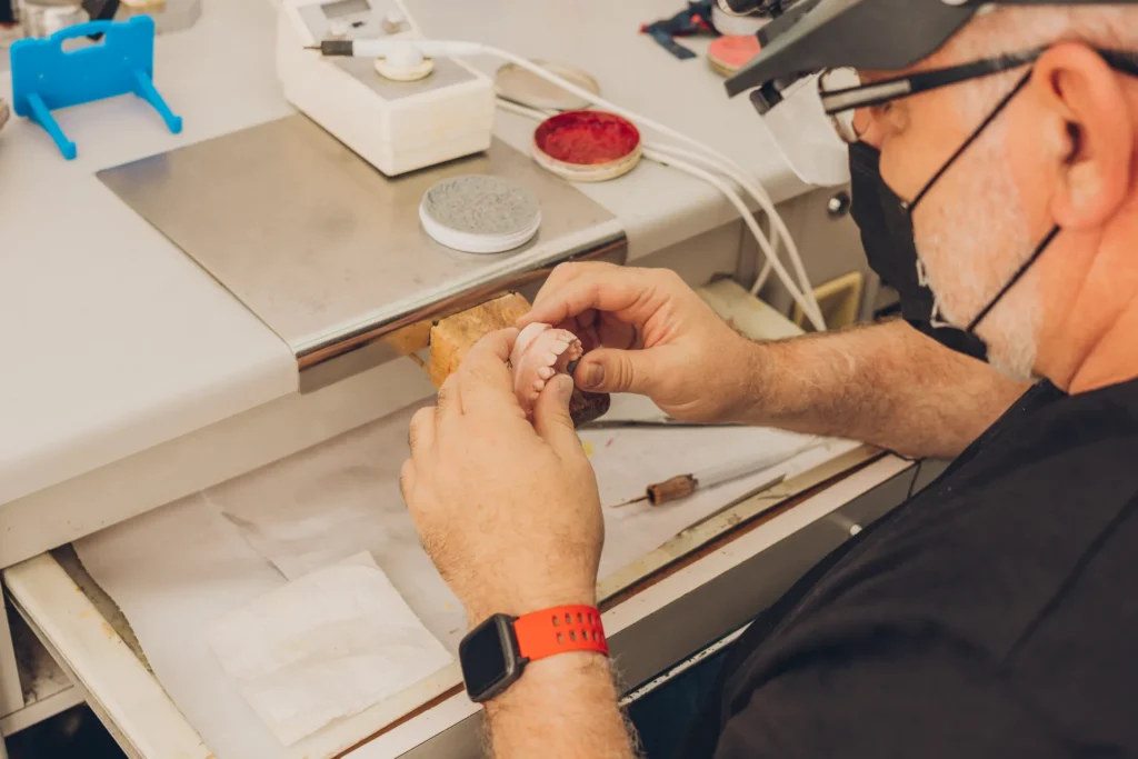 Tandtechnicus met loepbril werkt een prothese af